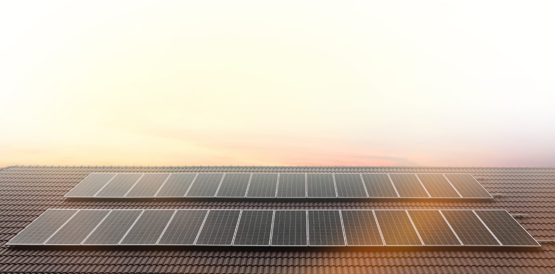 persoenlich_beraten_2 Zwei Reihen von Solarmodulen auf einem Ziegeldach mit einem weichen, hellen Himmel im Hintergrund, der einen Sonnenauf- oder -untergang andeutet.